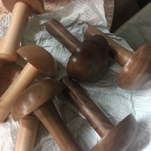 May include: A collection of wooden mushroom-shaped objects in various shades of brown and natural wood. The mushrooms have a smooth, polished finish and are arranged on a white surface.