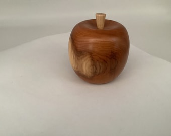 May include: A wooden apple sculpture with a smooth, brown finish and a light brown stem. The apple is sitting on a white surface.