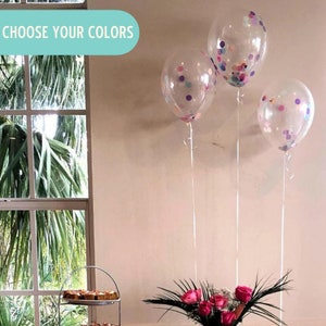 May include: Three clear balloons with confetti inside. The confetti is in shades of pink, purple, and blue. The balloons are tied together with white ribbon and are floating in the air. The text "CHOOSE YOUR COLORS" is visible in the top left corner of the image.