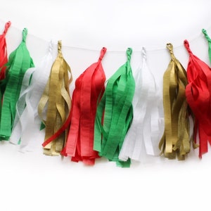 An arial shot of a Christmas themed tissue tassel garland sitting on a white table made up of red, green, white, and gold.