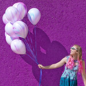 Girl smiling and holding a balloon bundle of ten 11 inch latex purple marble design balloons.