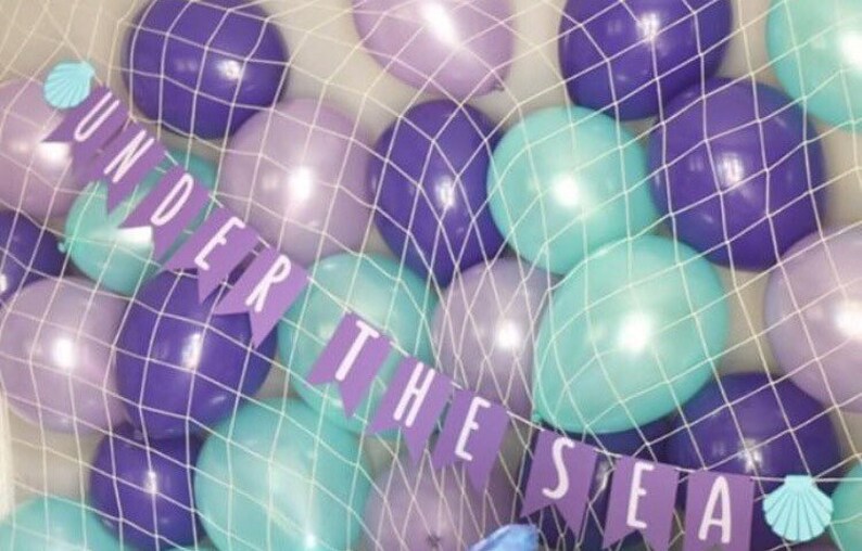 A fishing net holding a variety of balloons in purple, pearl lilac, and pearl mint.