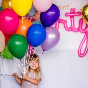 A little girl holding a bouquet of balloons in a variety of colors for her birthday.