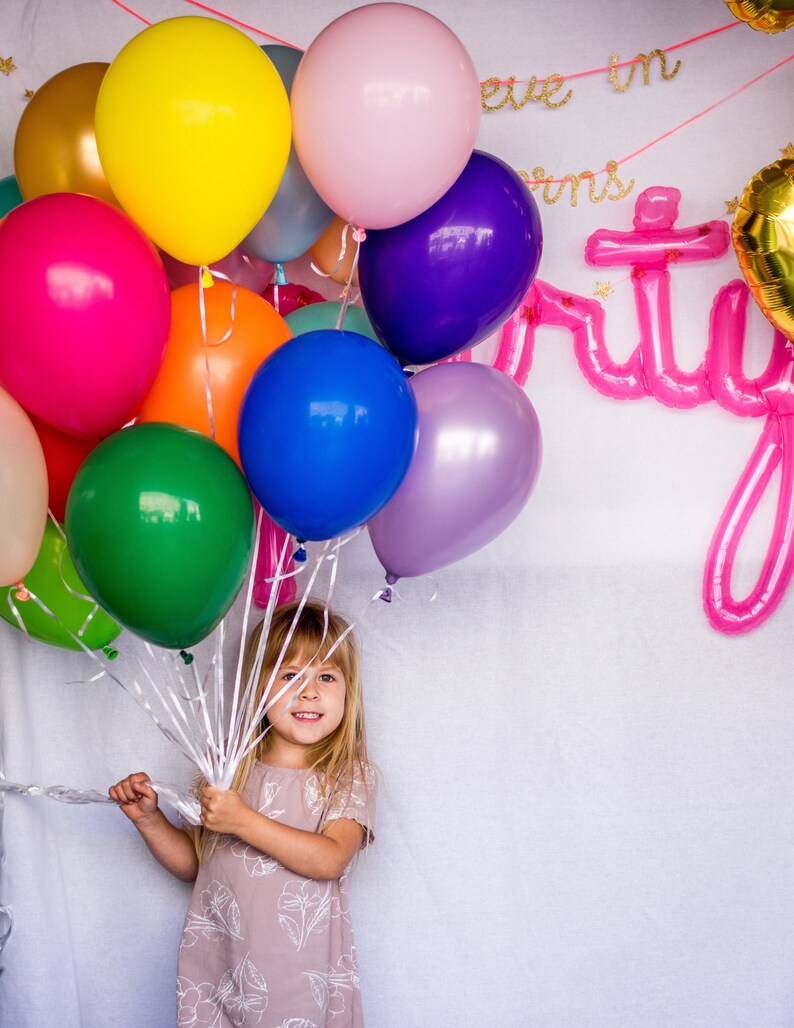 A little girl holding a bouquet of balloons in a variety of colors for her birthday.