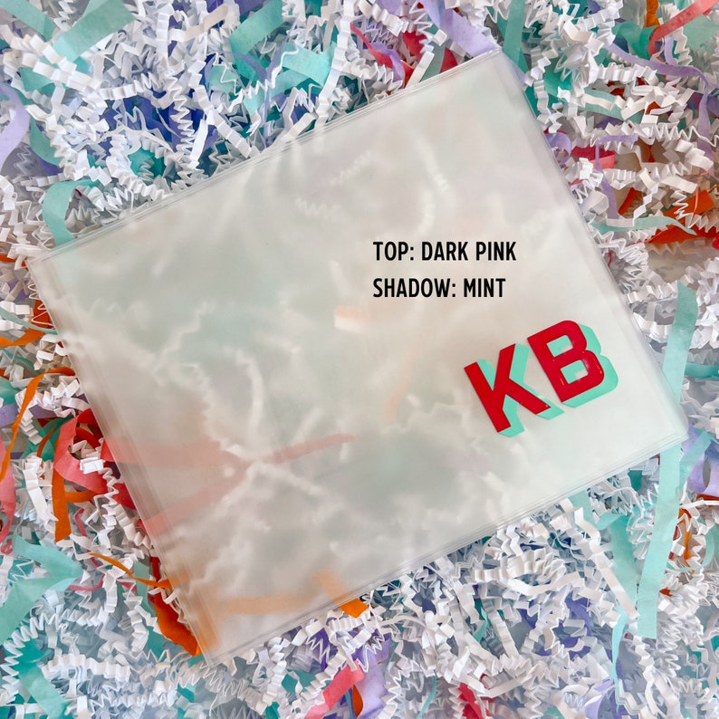 May include: A clear plastic envelope with the text "TOP: DARK PINK SHADOW: MINT" and the letters "KB" in red and turquoise.