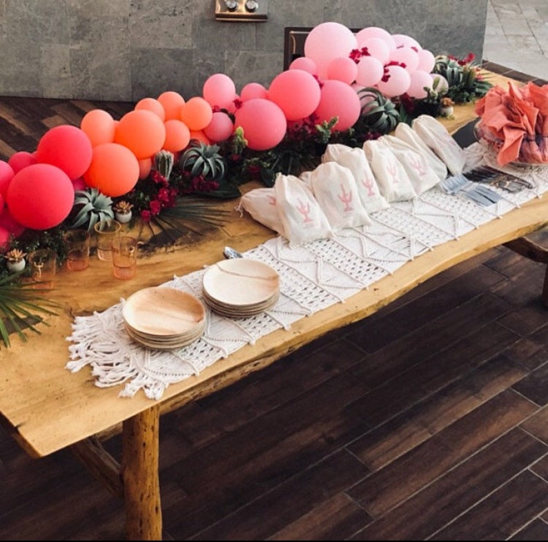 A balloon garland sits atop a bed of florals running along the middle of a wooden table.  The balloon garland is made up of wildberry, coral, rose, and pink balloons.