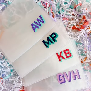 May include: Four clear plastic pouches with different colored letters on each. The letters are in a 3D style and spell out "AW", "MP", "KB", and "GVH".