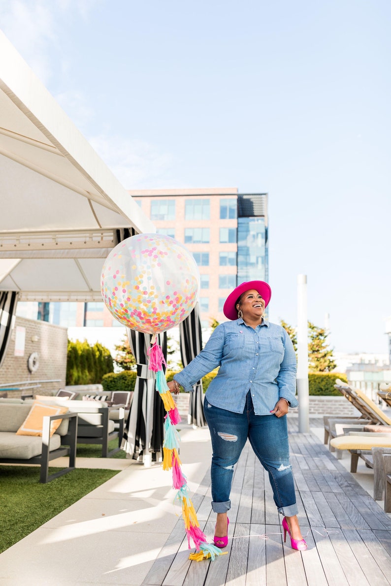 Woman smiling holding a jumbo 3ft clear balloon stuffed with tissue confetti.