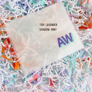 May include: A clear plastic bag with the text "TOP: LAVENDER SHADOW: MINT" and the letters "AW" in purple and turquoise.