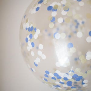 Close up of giant 3ft clear balloon stuffed with tissue confetti in the colors blue, white, and gold.