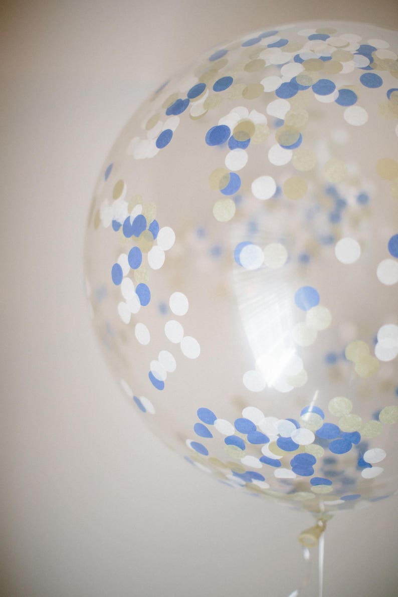 Close up of giant 3ft clear balloon stuffed with tissue confetti in the colors blue, white, and gold.