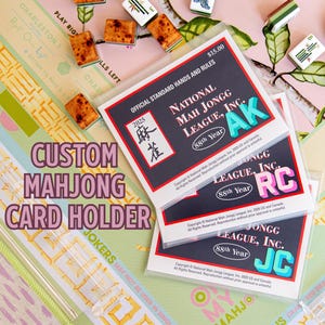 May include: A custom Mahjong card holder with the text "Custom Mahjong Card Holder" in a purple font. The image also shows Mahjong tiles and cards from the National Mah Jongg League, Inc.