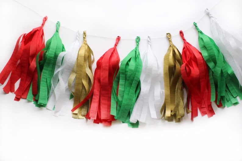 An arial shot of a Christmas themed tissue tassel garland sitting on a white table made up of red, green, white, and gold.