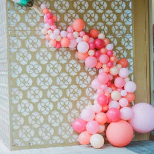 A tall wall with a champagne bottle balloon at the top left corner and pink, coral, and dark pink balloons in different sizes cascading out of the champagne bottle balloon.