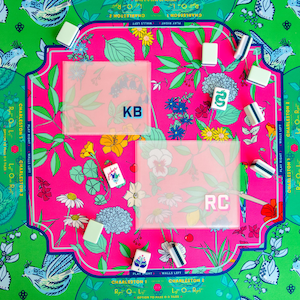 May include: A colorful Mahjong game set with a vibrant floral and bird design. The game board features a pink center with the initials "KB" and "RC" on clear covers. Green and white tiles are visible, along with floral and bird motifs.
