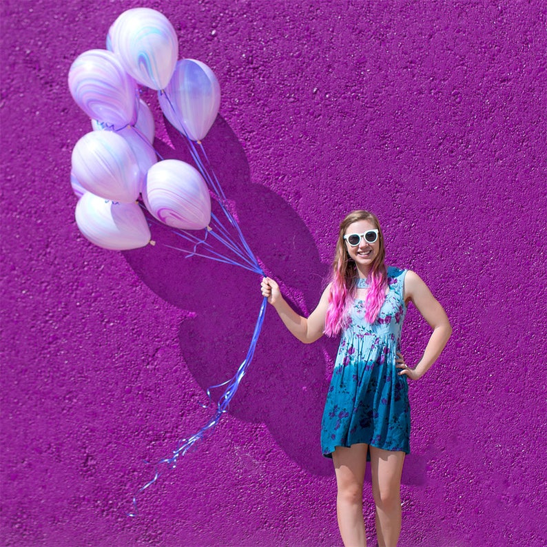 Girl smiling and holding a balloon bundle of ten 11 inch latex marble design balloons.