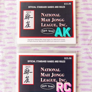 May include: Two National Mah Jongg League, Inc. rule cards. Each card has a black background with white text, including "Official Standard Hands and Rules" and "2025". The cards also feature the text "AK" and "RC" in bright colors.