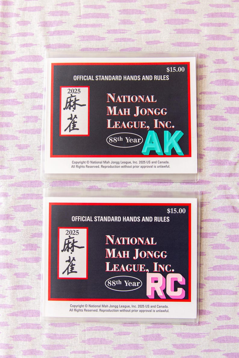 May include: Two National Mah Jongg League, Inc. rule cards. Each card has a black background with white text, including "Official Standard Hands and Rules" and "2025". The cards also feature the text "AK" and "RC" in bright colors.