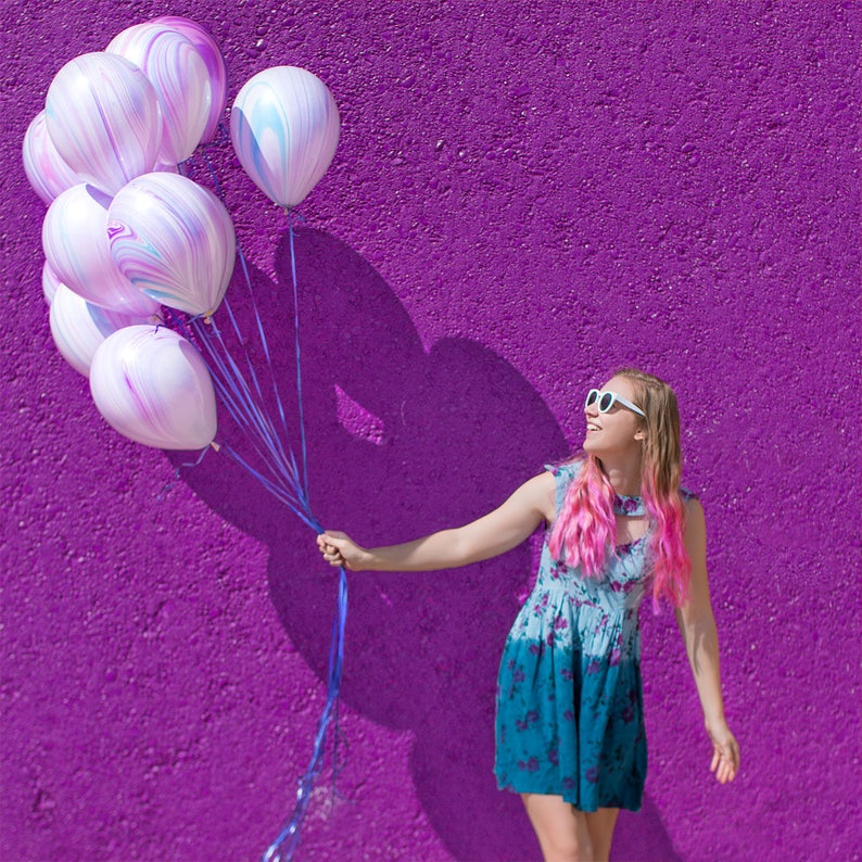 Girl smiling and holding a balloon bundle of ten 11 inch latex purple marble design balloons.