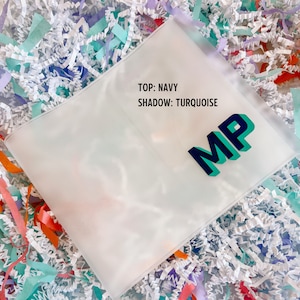 May include: A clear plastic envelope with the text "TOP: NAVY SHADOW: TURQUOISE" and the letters "MP" in turquoise with a navy blue outline.