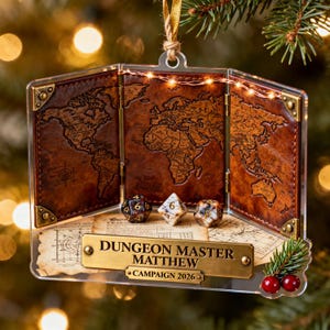 May include: A three-paneled brown leather-textured ornament featuring a world map, three polyhedral dice, and a brass-colored plaque reading DUNGEON MASTER MATTHEW and CAMPAIGN 2026. The piece is accented with gold metal corners and a string of lights.