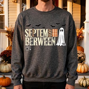 Può includere: Una felpa girocollo grigio scuro mélange con la scritta SEPTEM-BERWEEN in un mix di stampa leopardata, motivi a quadri e tinte unite. Il design include sagome nere di pipistrelli in volo, un fantasma bianco e una ragnatela grafica.