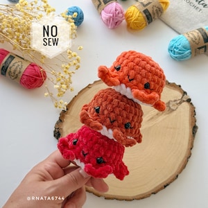 May include: Three handmade crochet octopus toys in shades of red and orange, stacked on top of each other. The toys have black eyes and white accents. The image also shows spools of yarn and the text "NO SEW".