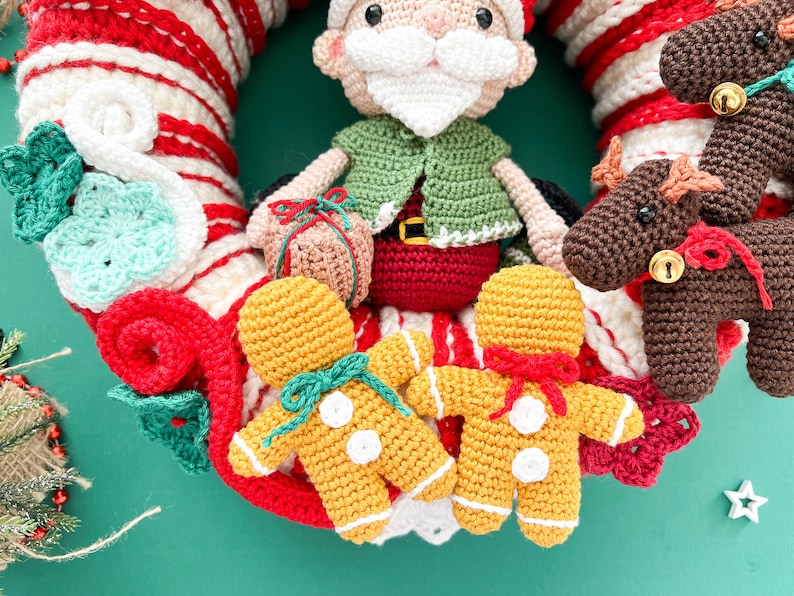 May include: A crocheted Christmas wreath with a Santa Claus, two gingerbread men, and a reindeer. The wreath is decorated with red and white stripes and green and white crocheted flowers.