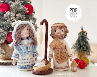 May include: Crochet nativity set featuring a figure in a white and blue dress with a head covering, a figure in a white and tan robe, and a small baby in a brown cradle under a brown shepherd's crook. Text reads PDF ENGLISH ONLY.