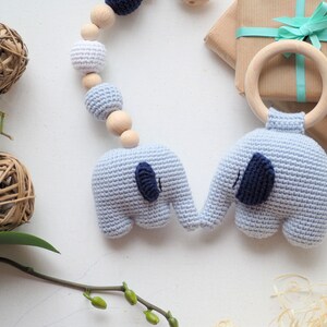 Puede incluir: Un sonajero para beb&eacute; de elefante tejido en azul y blanco con un aro de madera. El sonajero est&aacute; unido a una cadena de cuentas de madera con cuentas tejidas en blanco y azul.