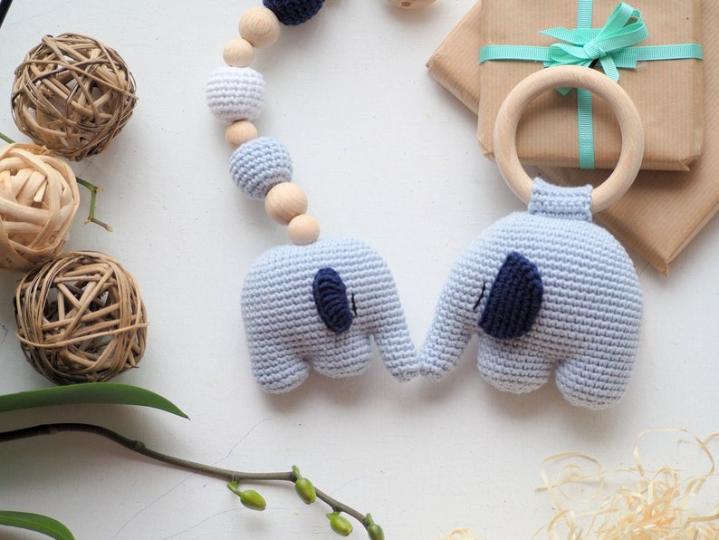 Puede incluir: Un sonajero para beb&eacute; de elefante tejido en azul y blanco con un aro de madera. El sonajero est&aacute; unido a una cadena de cuentas de madera con cuentas tejidas en blanco y azul.
