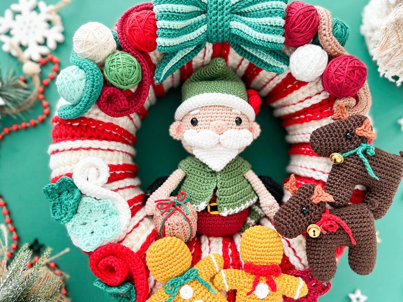 May include: A crocheted Christmas wreath with a red and white candy cane stripe design. The wreath is decorated with a green and white bow, a crocheted elf, gingerbread people, and reindeer.