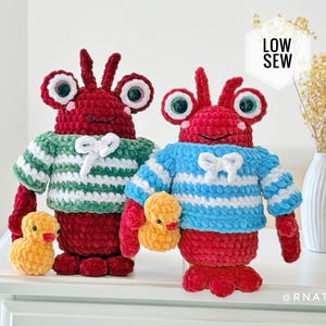 Puede incluir: Dos peluches de langosta tejidos a mano con grandes ojos de plástico, uno con un suéter de rayas verdes y blancas y el otro con uno de rayas azules y blancas. Cada langosta sostiene un pequeño pato de ganchillo amarillo. El texto dice LOW SEW.