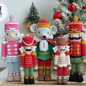 May include: A collection of handmade crochet Christmas ornaments, including nutcrackers and a mouse. The nutcrackers are in red, pink, and green, with detailed uniforms and mustaches. The ornaments are displayed in front of a Christmas tree.