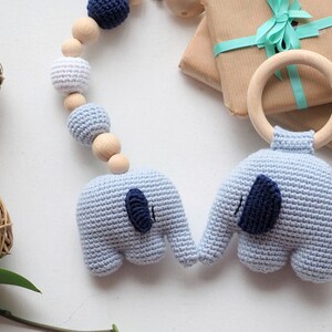 Puede incluir: Un juguete para beb&eacute; de crochet azul y blanco con dos figuras de elefantes y un anillo de madera. El juguete est&aacute; enhebrado con cuentas de madera y es perfecto para el desarrollo de un beb&eacute;.