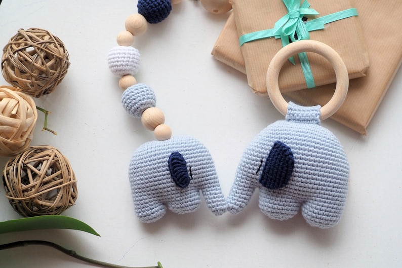 Puede incluir: Un juguete para beb&eacute; de crochet azul y blanco con dos figuras de elefantes y un anillo de madera. El juguete est&aacute; enhebrado con cuentas de madera y es perfecto para el desarrollo de un beb&eacute;.
