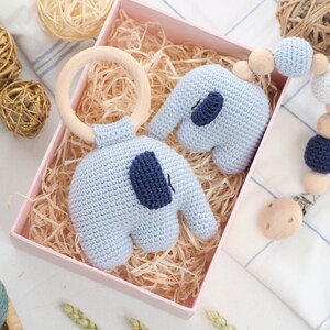 Puede incluir: Un conjunto de dos juguetes de elefante de crochet en azul claro con detalles azules. Un elefante est&aacute; unido a un anillo de madera y el otro es parte de un mordedor de cuentas de madera y clip.