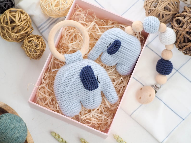 Puede incluir: Un conjunto de dos juguetes de elefante de crochet en azul claro con detalles azules. Un elefante est&aacute; unido a un anillo de madera y el otro es parte de un mordedor de cuentas de madera y clip.