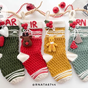 Puede incluir: Cuatro calcetines de Navidad tejidos a crochet en verde, rojo, amarillo y verde con ribetes blancos. Cada calcetín tiene un adorno diferente: un corazón, un reno, un hombre de jengibre y un árbol de Navidad. Los calcetines están colgados de una rama con un fondo blanco.