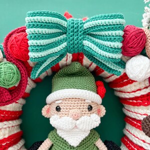 May include: A crocheted Christmas wreath with a green and white striped bow, red and white candy cane stripes, and a crocheted gnome wearing a green hat and white beard.