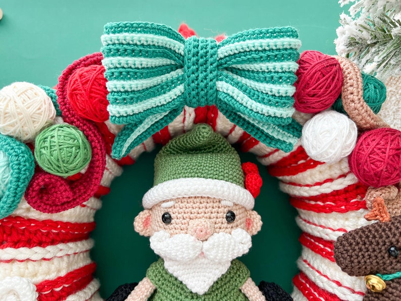 May include: A crocheted Christmas wreath with a green and white striped bow, red and white candy cane stripes, and a crocheted gnome wearing a green hat and white beard.