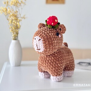 May include: A handmade brown crochet animal with a strawberry hat. The plush toy has a light pink face and feet. A small vase with yellow flowers is in the background.