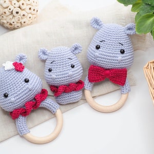 May include: Three handmade crochet hippo baby rattles. The hippos are light grey with red bow ties and wooden ring handles. One hippo has a white and red flower. The rattles are designed for babies and are soft and safe.