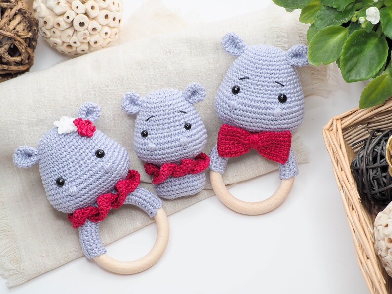 May include: Three handmade crochet hippo baby rattles. The hippos are light grey with red bow ties and wooden ring handles. One hippo has a white and red flower. The rattles are designed for babies and are soft and safe.