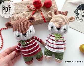 May include: Two crocheted reindeer toys wearing red and white striped sweaters and green trousers. The reindeer have brown and white fur and are standing on a white surface.