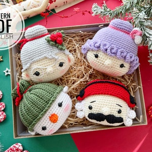 May include: Four crocheted Christmas ornaments in a box. The ornaments are a snowman, a woman with a purple hat, a man with a red hat, and a woman with a gray hat. The ornaments are all smiling and have black eyes.
