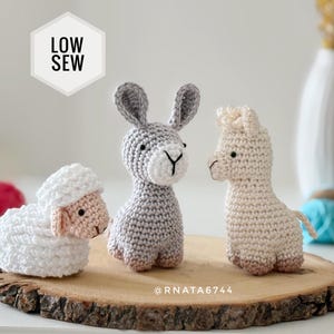 May include: Three crocheted animal figures including a white sheep, a gray donkey, and a cream-colored llama. A white hexagon graphic in the upper left corner contains the black text LOW SEW. The text @RNATA6744 is printed in white near the base.