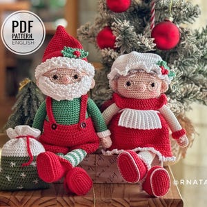 May include: Two crocheted dolls, one resembling Santa Claus in a red hat and green shirt, and one in a white bonnet and red dress. A small green gift bag with white snowflake patterns sits beside them. A circular icon reads PDF PATTERN ENGLISH.