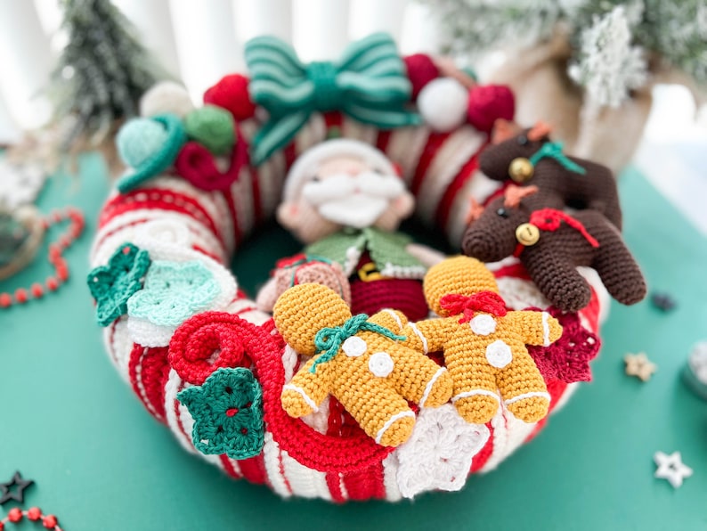 May include: A crocheted Christmas wreath with a red and white candy cane stripe pattern. The wreath is decorated with crocheted gingerbread people, a Santa Claus, a bow, and other festive ornaments.