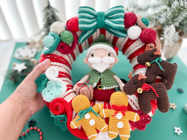 May include: A crocheted Christmas wreath with a red and white candy cane design. The wreath is decorated with a green and white bow, a green elf holding a gift, two gingerbread men, and two brown reindeer.